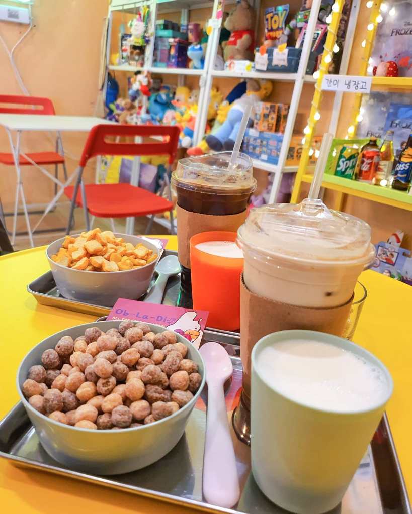 Two plates featuring an iced americano and French Toast Crunch and a latte and Trix (?)