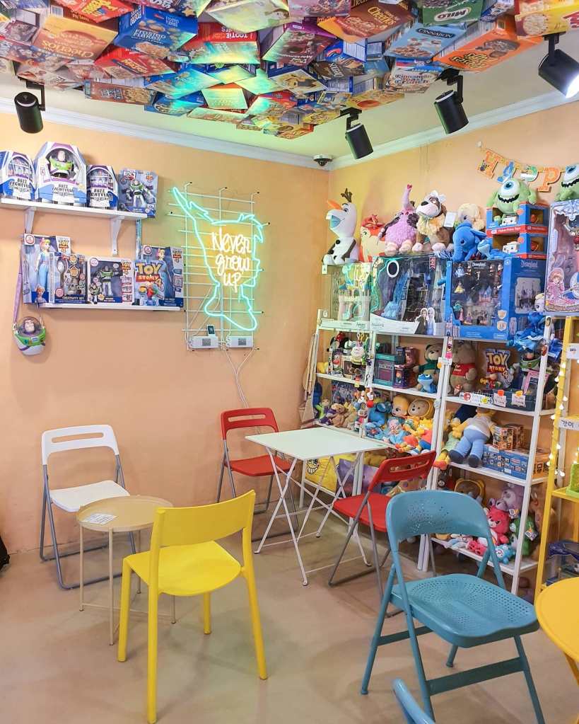 The corner of the cafe with the Peter Pan neon sign and three shelves bursting full of toys and stuffed animals